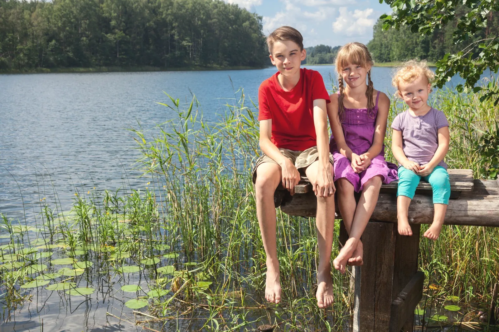 Three children sitting by a lake